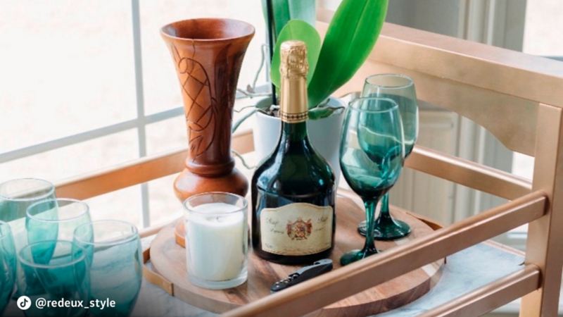 A bar cart with a bottle and glassware on top.