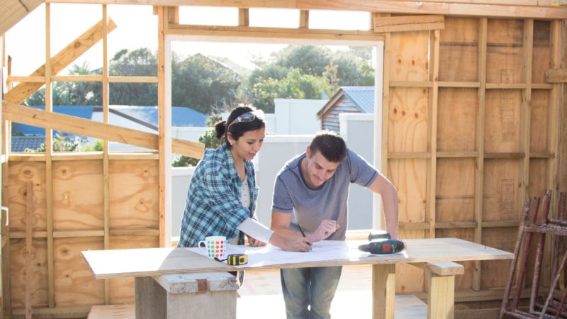 Two people look over plans at a work table while constructing a tiny house.