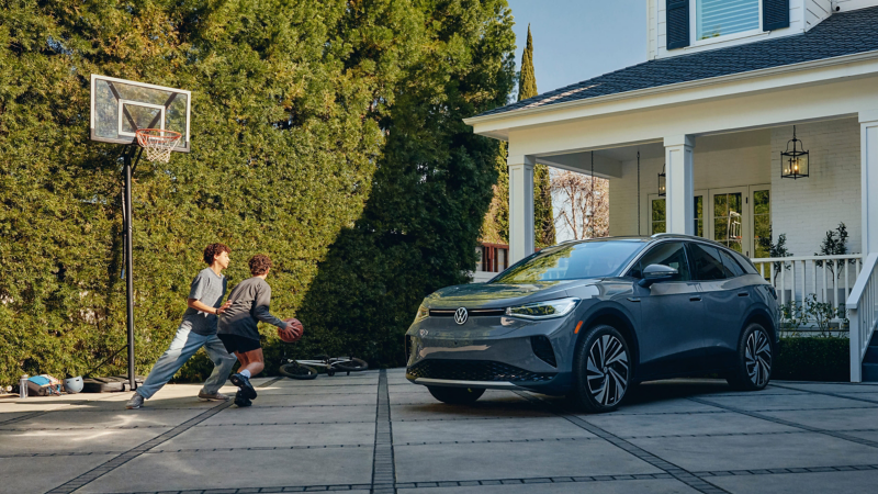 Un vehículo eléctrico ID.4 en color Pure Gray está estacionado en la entrada de una casa señorial, mientras dos niños juegan al baloncesto cerca de allí.