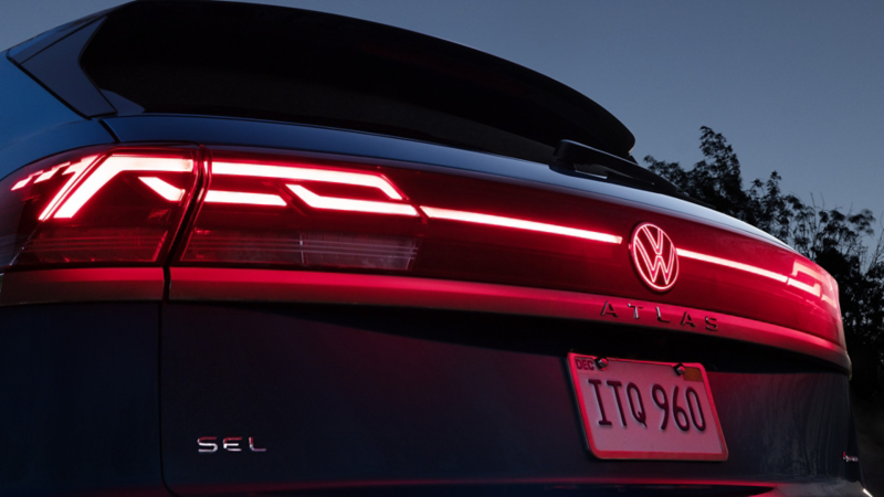 A close-up view of the LED taillights with illuminated light bar and emblem of the Atlas Cross Sport shown in Kingfisher Blue Metallic.
