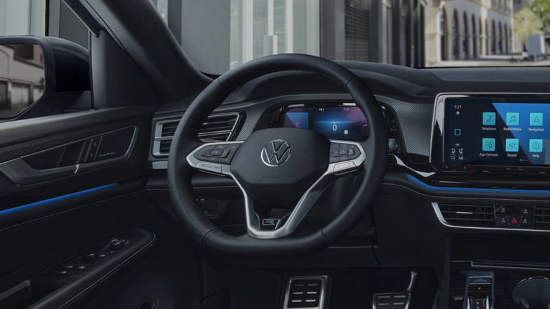 Interior view as seen from the driver POV of the steering wheel, front dash, gear shift and pedals of an Atlas Cross Sport with city buildings in the background.