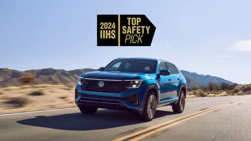 A front ¾ view of an Atlas Cross Sport shown in Kingfisher Blue Metallic driving on a wooded mountain road with a 2024 IIHS TOP SAFETY PICK graphic superimposed on image.