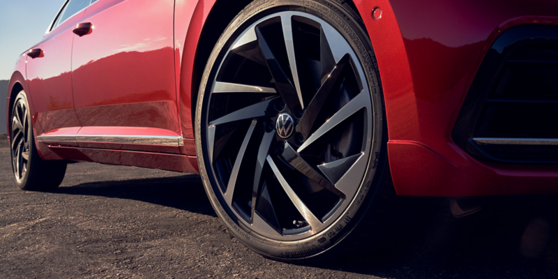 Close up of the available 20" alloy wheel on the front passenger side of an Arteon in Kings Red Metallic.