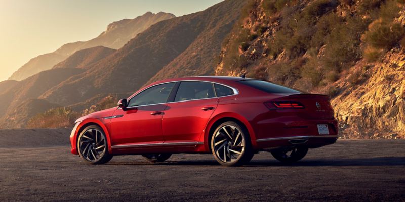 A profile shot of an Arteon shown in Kings Red Metallic, parked along a scenic overlook with foothills in the background. 