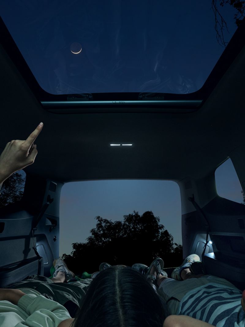 Night shot of a family in a parked Atlas looking up through the available panoramic sunroof at the stars in the night sky.