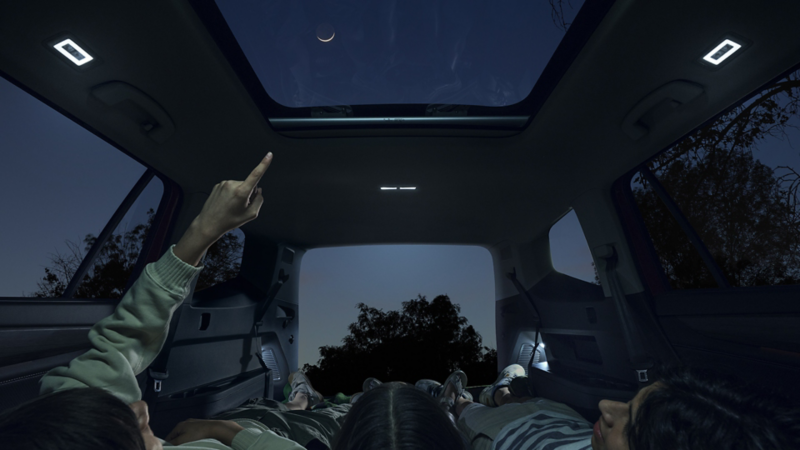 Night shot of a family in a parked Atlas looking up through the available panoramic sunroof at the stars in the night sky.