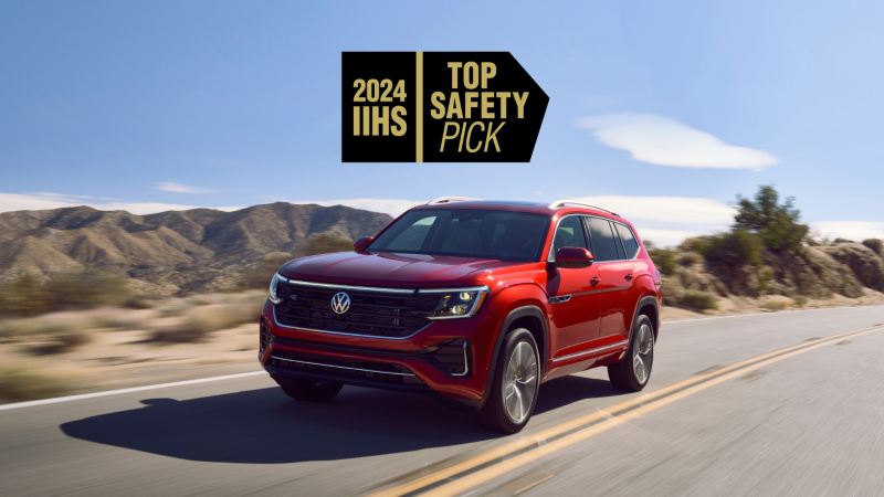 Front view of an Atlas in Aurora Red Metallic driving on a wooded mountain road with a 2024 IIHS TOP SAFETY PICK graphic superimposed on image.