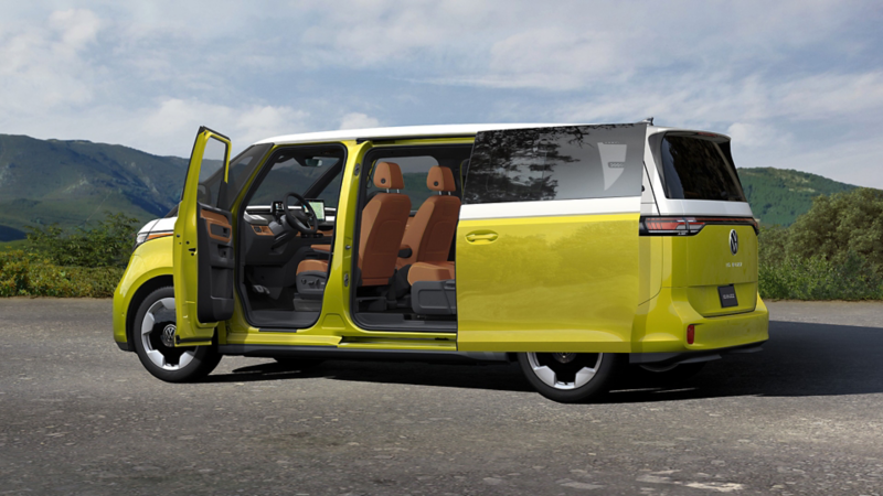 An ID. Buzz shown in Pomelo Yellow Metallic and Candy White with the front and side sliding doors open is parked with tree covered mountains in the background.