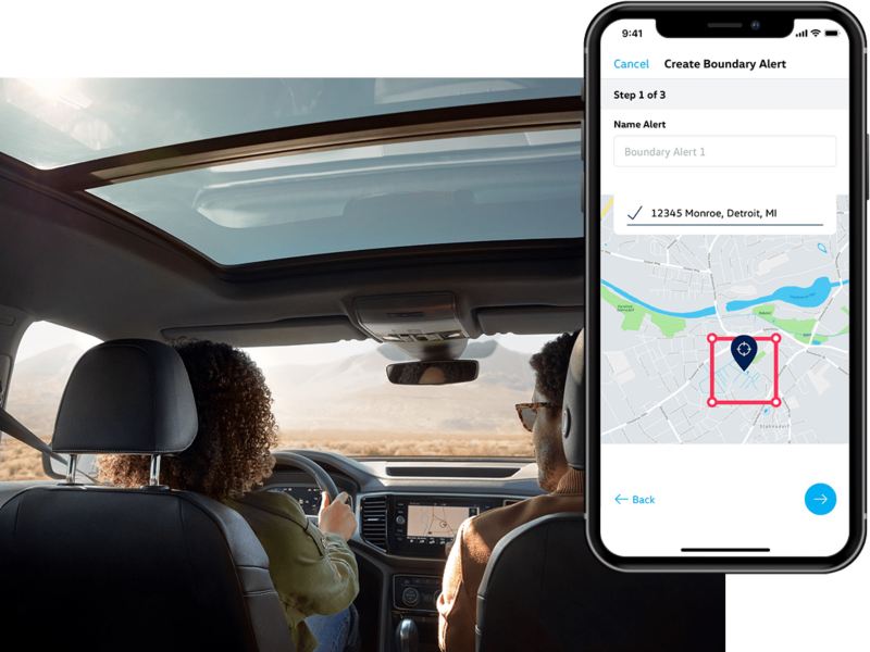 A man and woman review their Boundary Alert in their Car-Net app from their parked Volkswagen.