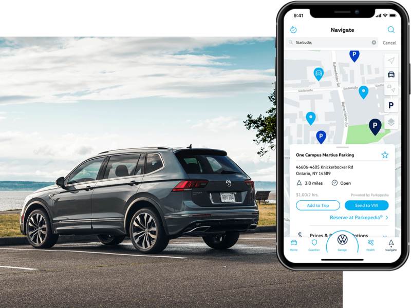 A Tiguan in Platinum Gray Metallic parked in front of a lake as seen from behind. On his phone, we see the in-app Volkswagen Car-Net® Remote Access Parking Info.