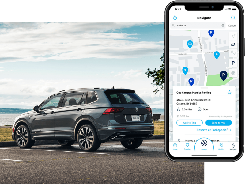 A Tiguan in Platinum Gray Metallic parked in front of a lake as seen from behind. On his phone, we see the in-app Volkswagen Car-Net® Remote Access Parking Info.
