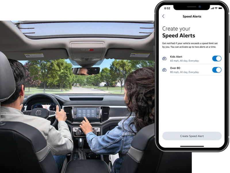 A man and woman sit in their VW with the MyVW app displayed on a superimposed mobile phone.
