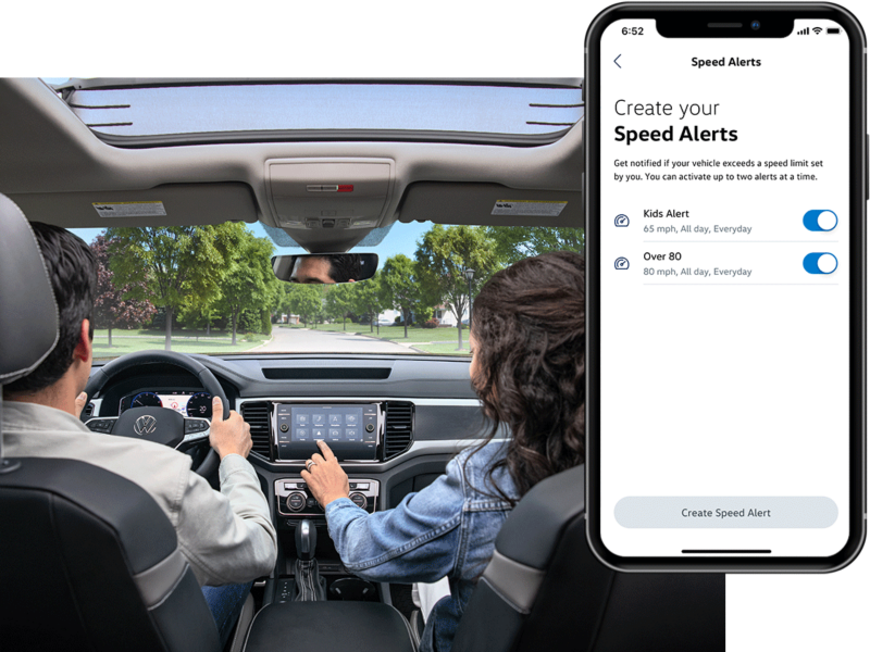 A man and woman sit in their VW with the MyVW app displayed on a superimposed mobile phone.
