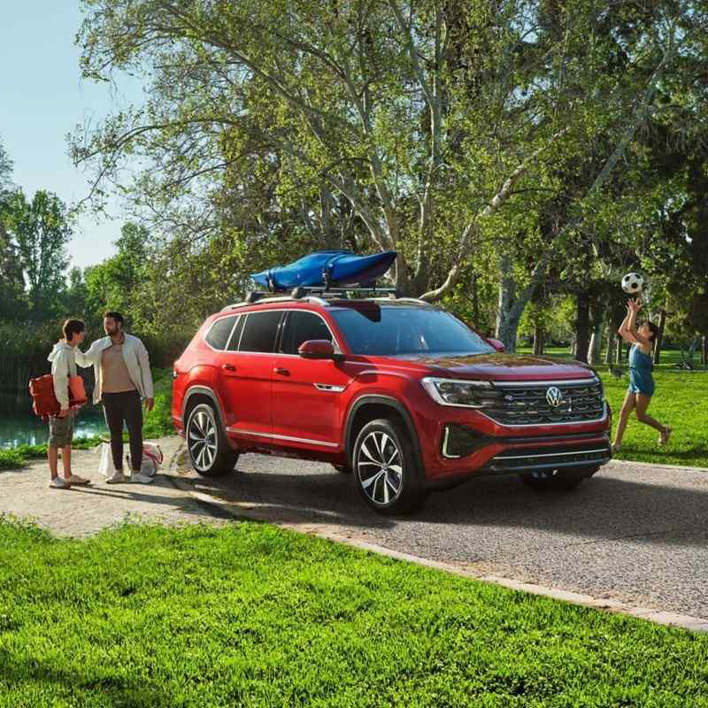 Atlas estacionado en la acera en un parque, con una familia disfrutando del parque y el lago al fondo.
