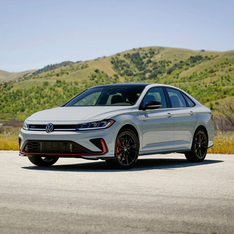 Front ¾ view of a Jetta GLI shown in Monument Gray with wooded hills in the background. 