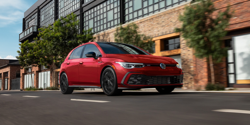 Front view of a Golf GTI shown in Kings Red Metallic driving on an urban street.