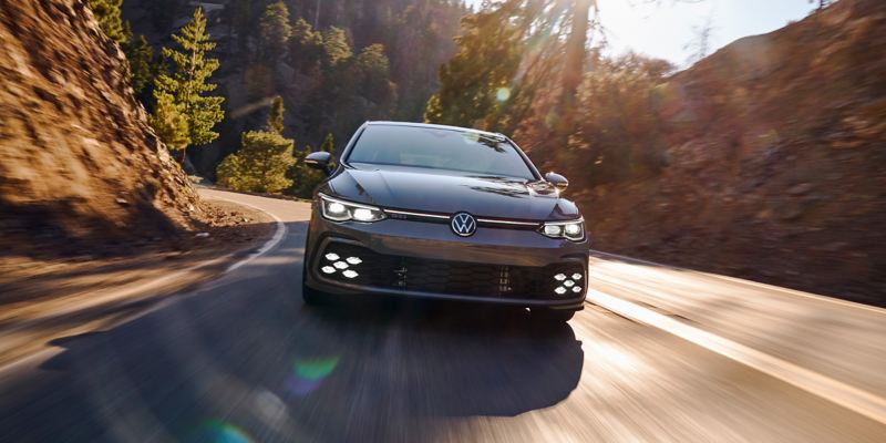 Moonstone Gray Golf GTI accelerates out of a corner on a hilly, wooded road.