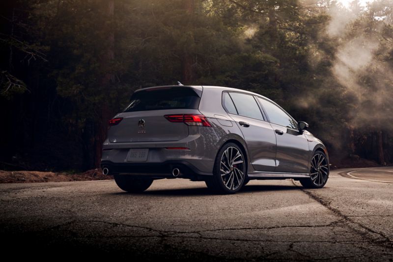 Golf GTI shown in Moonstone Gray from the rear, parked off a tree-lined road at dawn.