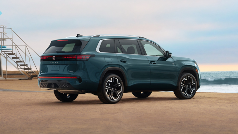 Rear side view of an Atlas shown in Sacramento Green Metallic parked with the ocean in the background. 