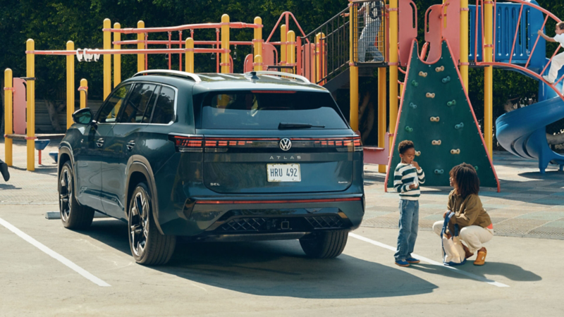 An Atlas shown in Sacramento Green Metallic is parked next to a playground while a mom and son talk nearby the Atlas.