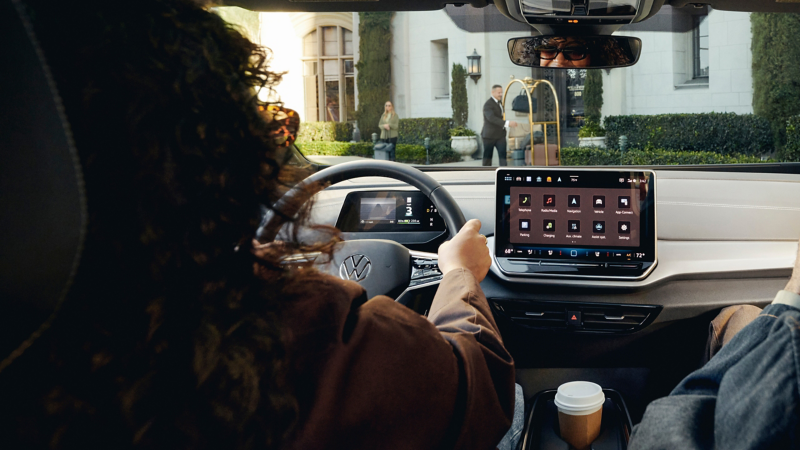 Interior view looking over the shoulder of a person driving an ID.4 electric vehicle with an upscale hotel visible through the windshield. 