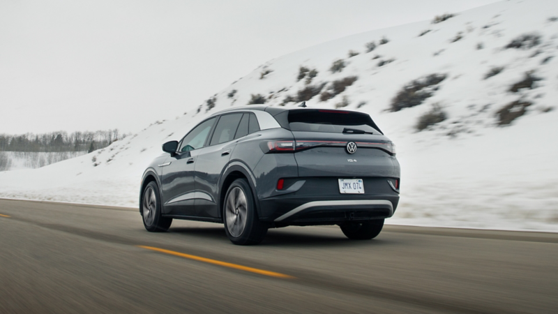 A rear ¾ view of the ID.4 shown in Pure Gray driving on a road with snow covered hills in the background.