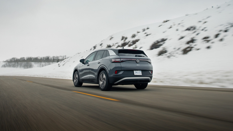 A rear ¾ view of the ID.4 shown in Pure Gray driving on a road with snow covered hills in the background.