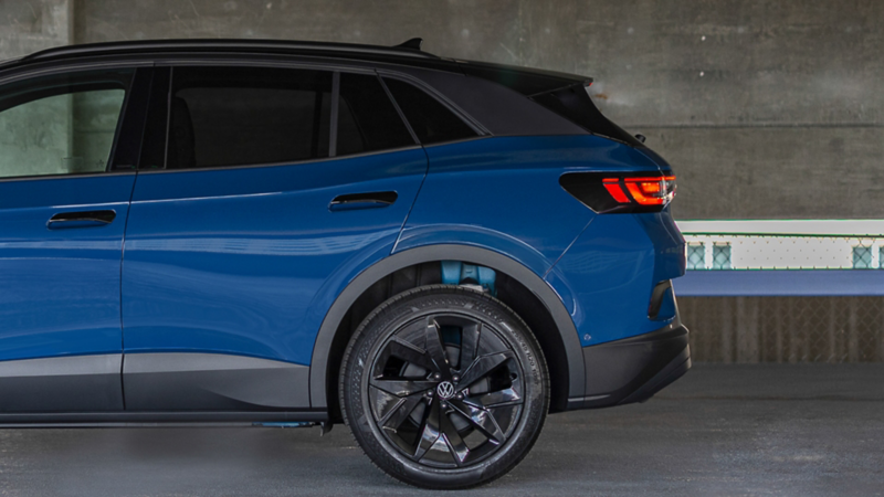 Extremo posterior de una vista de perfil lateral del ID.4 en color Mountain Lake Blue Metallic, estacionado en un entorno industrial.