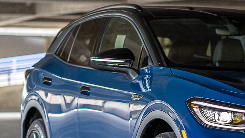 Partial frontal 3/4 image of ID.4 in Mountain Lake Blue Metallic parked on a industrial setting.