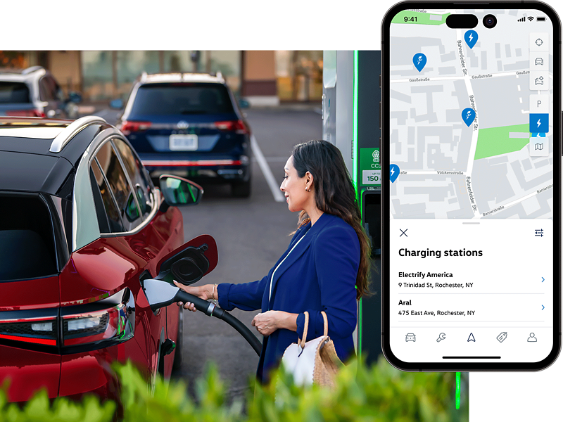 A well-dressed woman, parked at charging station stands on the passenger side of an ID.4 SUV in Aurora Red Metallic plugging a charging cable into the vehicle. The MyVW app is displayed on a superimposed mobile phone.