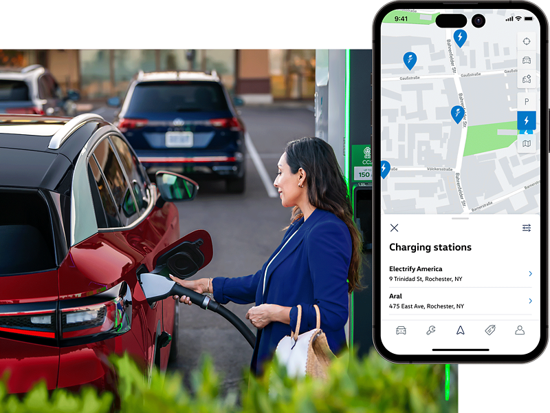 A well-dressed woman, parked at charging station stands on the passenger side of an ID.4 SUV in Aurora Red Metallic plugging a charging cable into the vehicle. The MyVW app is displayed on a superimposed mobile phone.