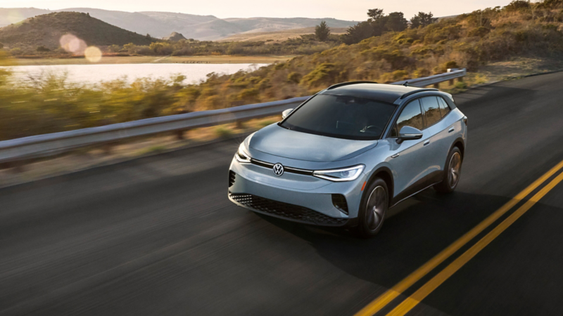 Front view of an ID.4 shown in Arctic Blue Metallic driving with mountains and a lake in the background.