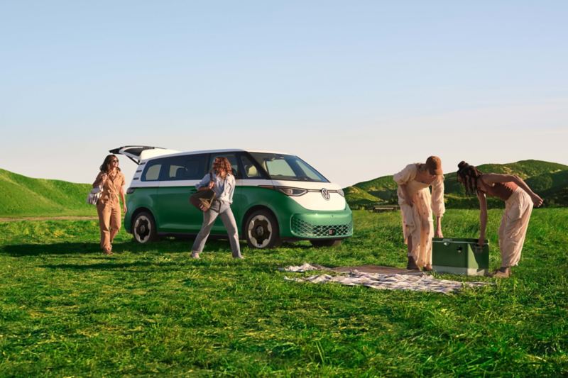 An ID. Buzz shown in Mahi Green Metallic in a grassy field with people outside the vehicle preparing to enjoy the outdoors.