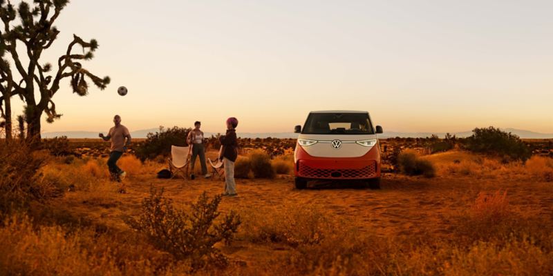 An ID. Buzz shown in Energetic Orange Metallic in a desert landscape with people outside the vehicle preparing to enjoy the outdoors.