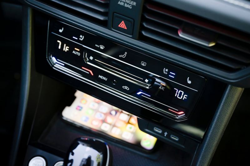 Jetta GLI air conditioning controls with a phone charging in the center console charging pad for compatible devices.