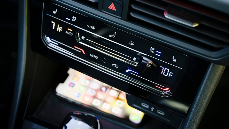 Controles del aire acondicionado del Jetta GLI con un teléfono cargándose en la almohadilla de carga disponible en la consola central para dispositivos compatibles