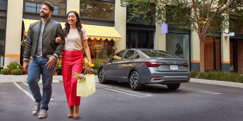 Two people walk away from a Jetta shown in Platinum Gray Metallic parked in front of a flower store.