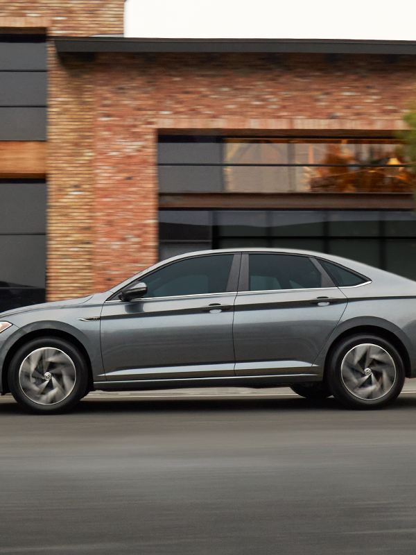 Jetta shown in Platinum Gray Metallic as seen from the front driving on a modern city street.