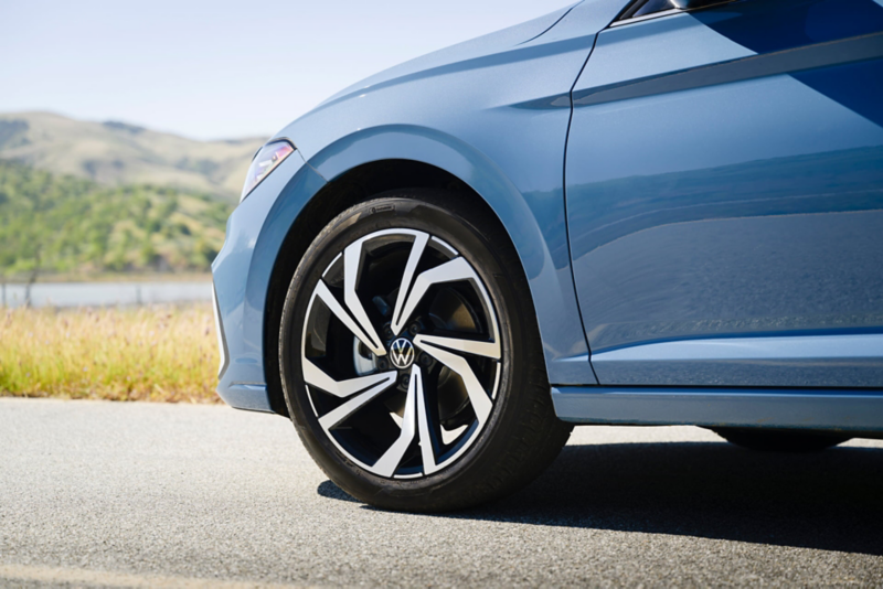 Close up view of available 17” alloy wheels on a Jetta shown in Monterey Blue Pearl parked with wooded hills in the background. 