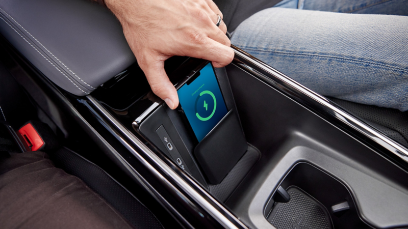 Person holding a phone charging in the available center console charging pad for compatible devices