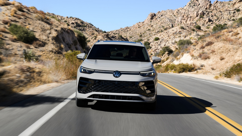 Head-on view of a Tiguan shown in Sandstone driving on a mountain road with rocks and shrubs making up the landscape.
