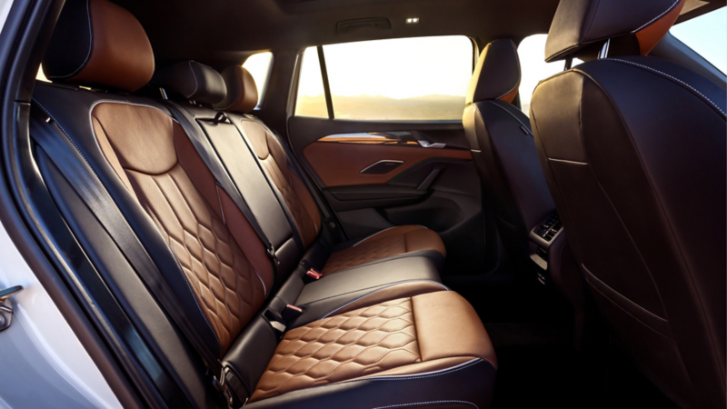 Interior view of the rear seats in a Tiguan shown in available Amber Brown leather looking from passenger's side with mountains at sunset visible through the windows.