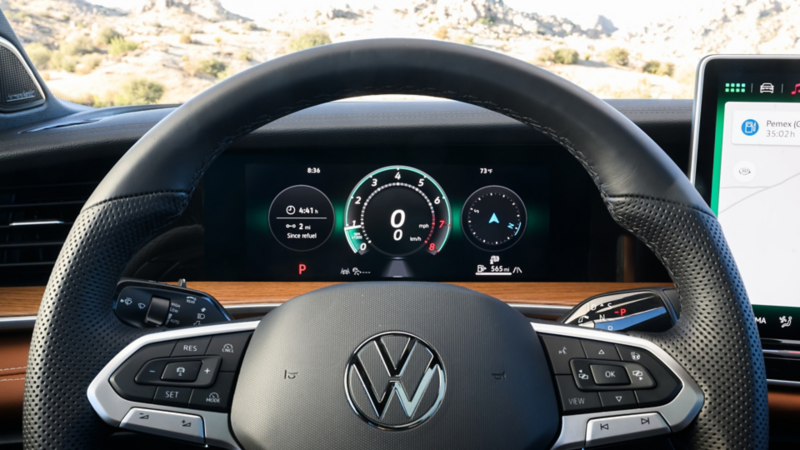 Close up view of the VW Digital Cockpit Pro and available heated steering wheel in a Tiguan with rocky mountains visible through the windshield.