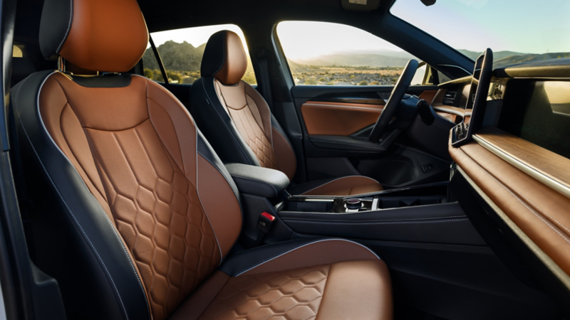 Vista interior de los asientos traseros de un Tiguan en cuero Amber Brown disponible, desde el lado del pasajero, con montañas al atardecer visibles a través de las ventanillas.