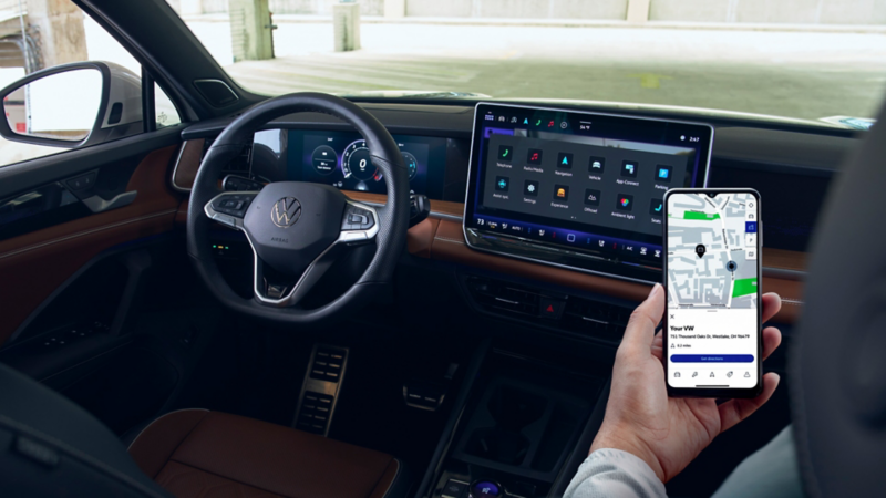 El pasajero delantero en un Tiguan estacionado sostiene un smartphone frente a la pantalla táctil central.