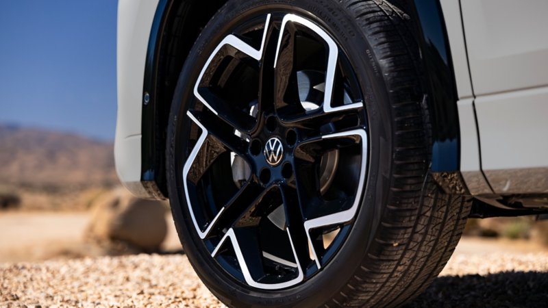 Close up view of the available 20" alloy wheels on a Tiguan shown in Sandstone parked in a desert setting.