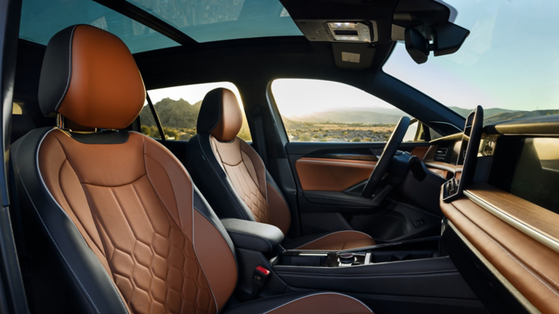 Vista interior de un Tiguan en cuero Amber Brown disponible, visto desde el lado del pasajero a través del tablero y por las ventanas del lado del conductor, con montañas y un valle visibles en el fondo.