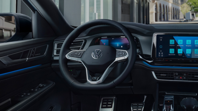 Interior view as seen from the driver POV of the steering wheel, front dash, gear shift and pedals of an Atlas Cross Sport with city buildings in the background.