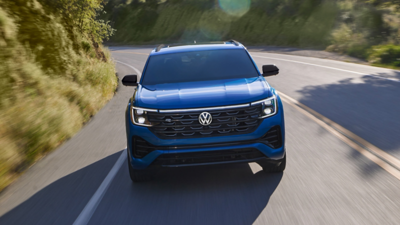A front view of an Atlas Cross Sport shown in Mountain Lake Blue driving on a wooded mountain road.