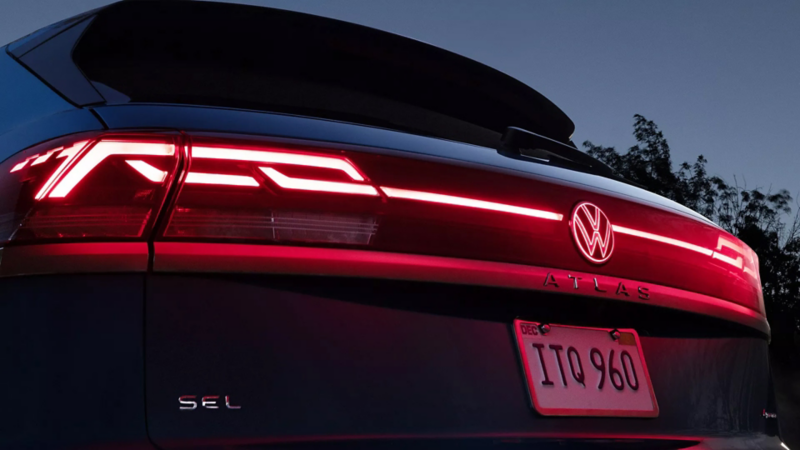 A close-up view of the LED taillights with illuminated light bar and emblem of the Atlas Cross Sport shown in Mountain Lake Blue.